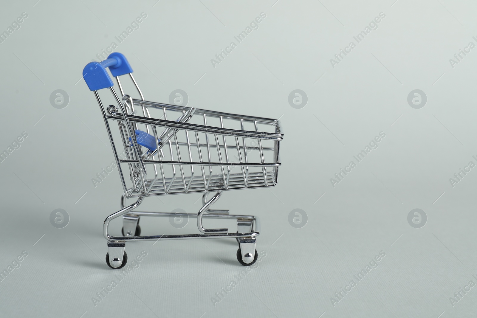 Photo of Small metal shopping cart on light background, space for text