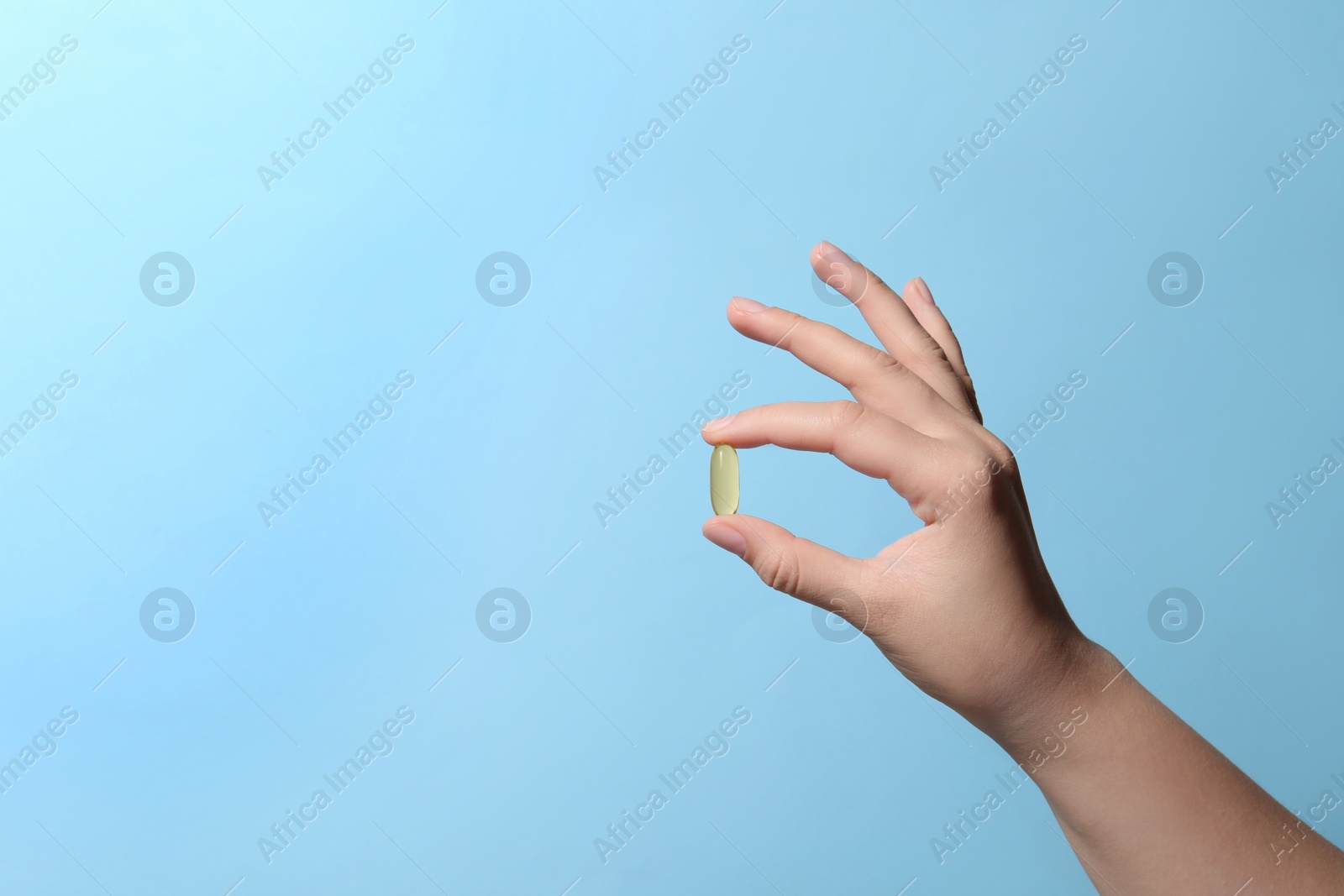 Photo of Woman holding pill on light blue background, closeup. Space for text