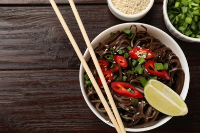 Photo of Tasty buckwheat noodles (soba) with chili pepper and sesame served on wooden table, flat lay. Space for text