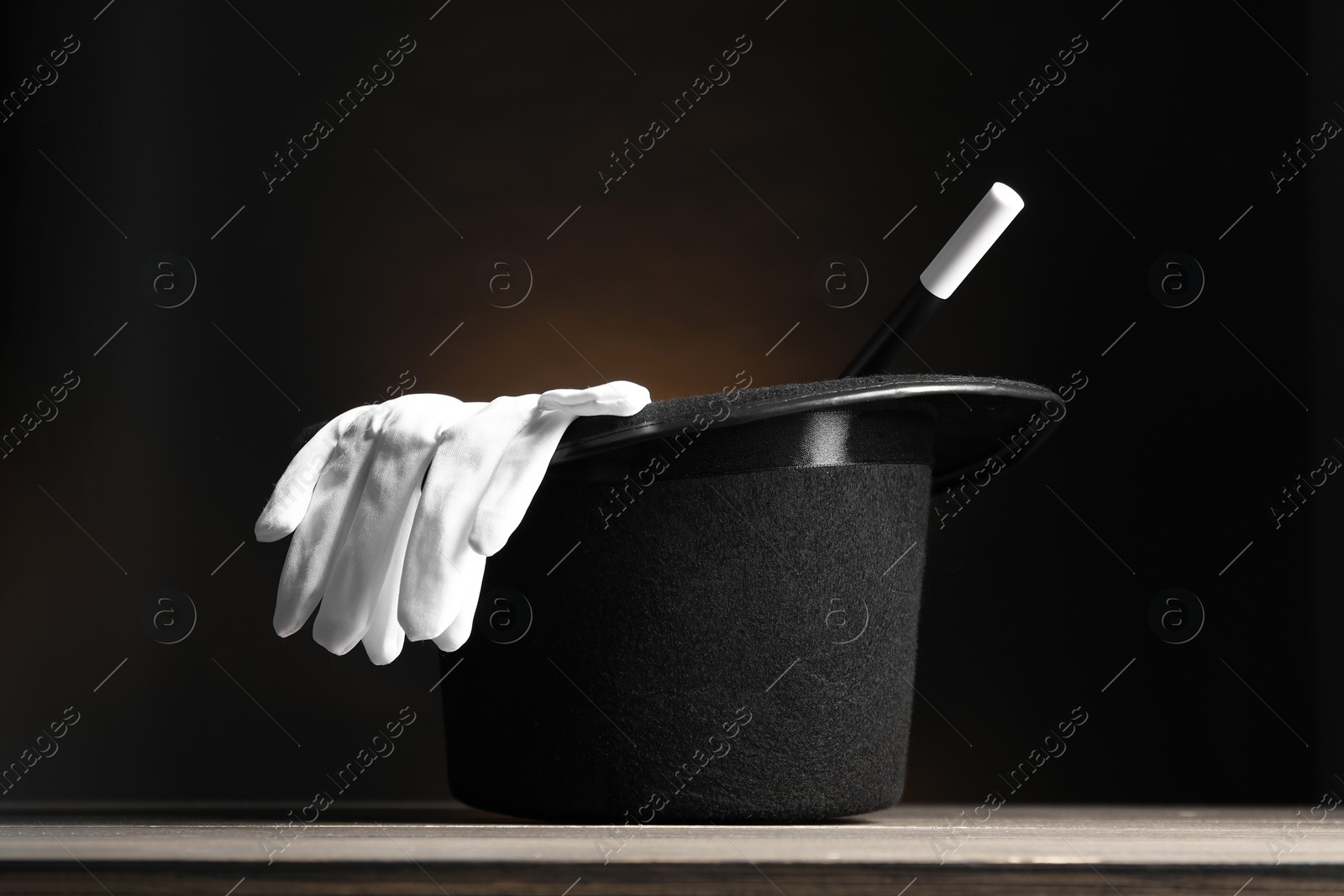 Photo of Magician's hat, gloves and wand on wooden table against dark background