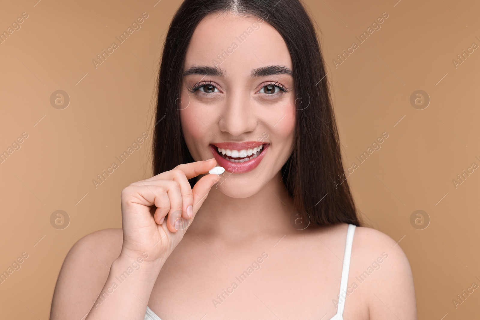 Photo of Beautiful young woman with vitamin pill on beige background