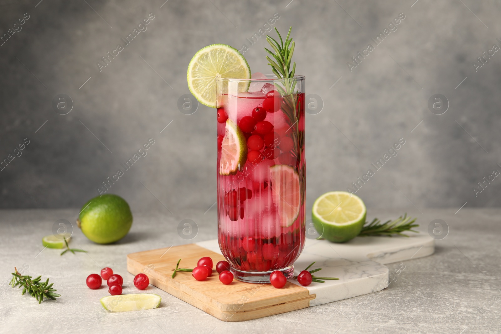 Photo of Tasty cranberry cocktail with rosemary and lime in glass on gray textured table