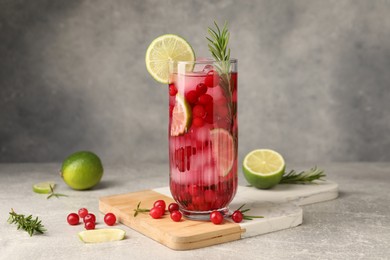 Photo of Tasty cranberry cocktail with rosemary and lime in glass on gray textured table
