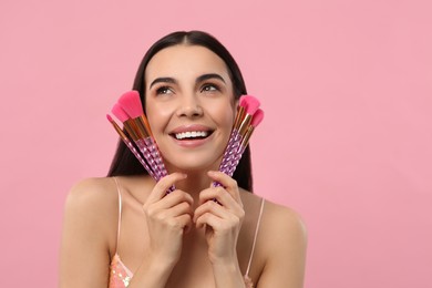 Happy woman with different makeup brushes on pink background. Space for text