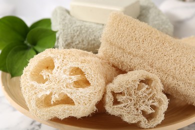 Photo of Loofah sponges, towel, soap and green leaves on table, closeup