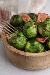 Delicious roasted Brussels sprouts and bacon in bowl on light table, closeup