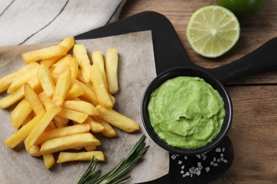 Photo of Serving board with french fries, avocado dip, rosemary and lime served on wooden table, top view