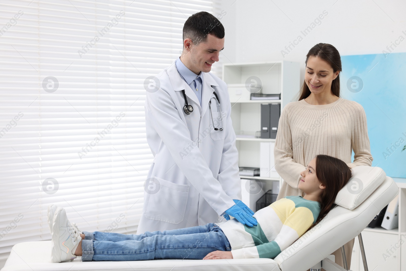 Photo of Gastroenterologist examining girl with stomach ache on couch in clinic