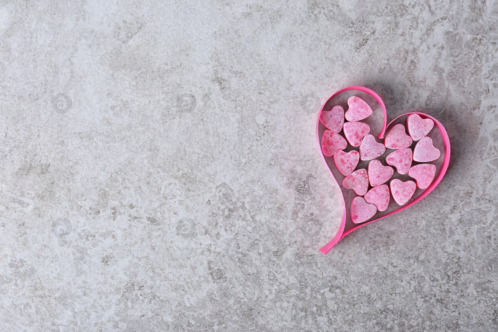 Photo of Small heart shaped candies with ribbon and space for text on gray background, top view