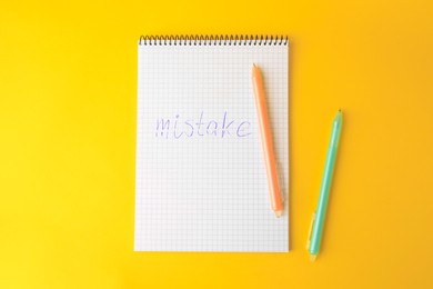 Photo of Word Mistake written in notepad with erasable pen on yellow background, flat lay