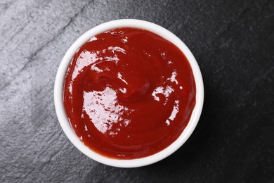 Organic ketchup in bowl on black table, top view. Tomato sauce