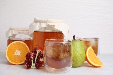 Tasty kombucha with ice cubes and fresh fruits on white tiled table