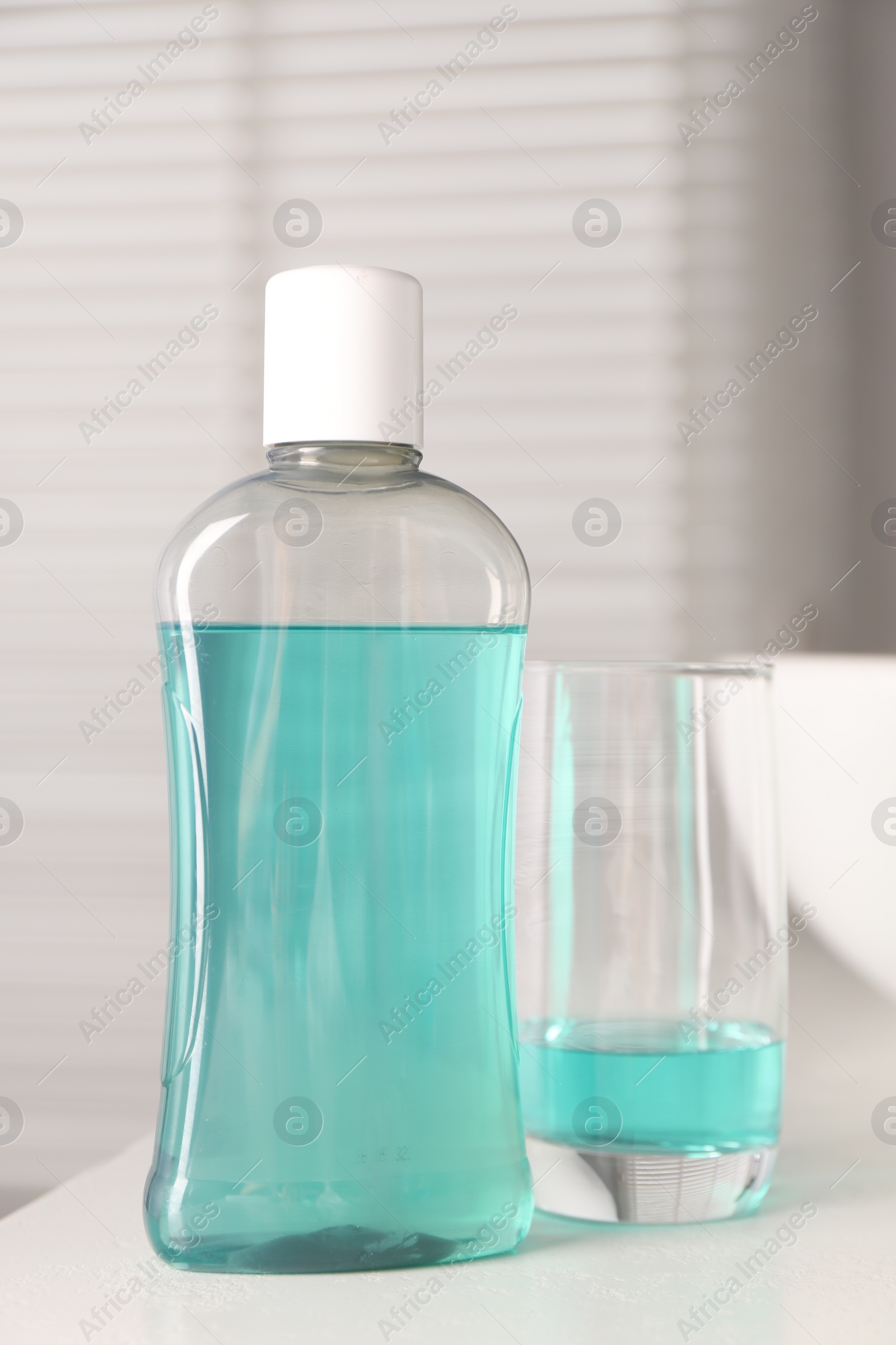 Photo of Bottle and glass of mouthwash on white countertop in bathroom