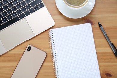 Photo of Empty notebook, laptop, coffee and smartphone on wooden table, flat lay