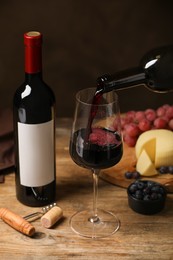 Photo of Pouring red wine into glass and appetizers on wooden table