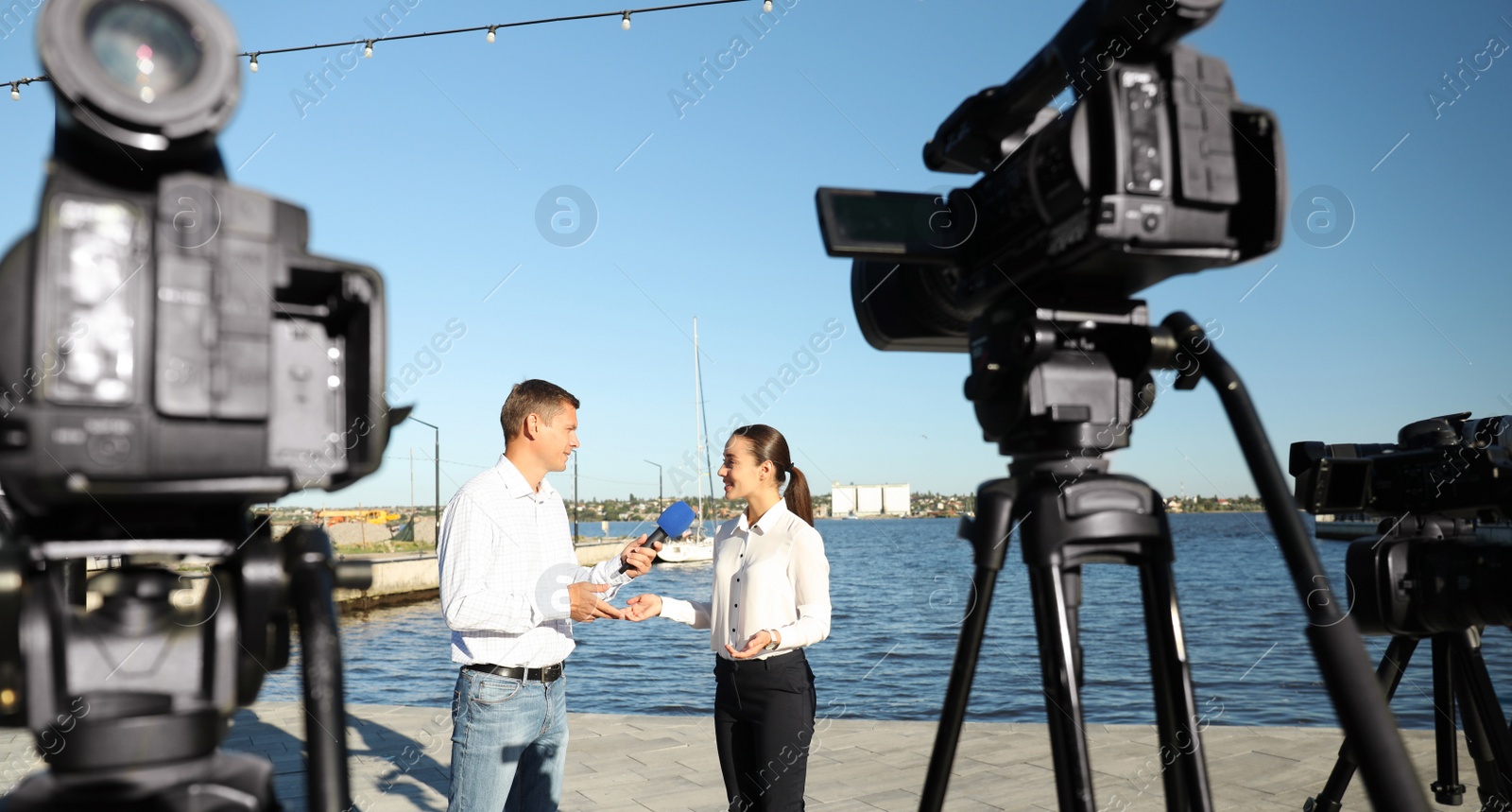 Photo of Professional journalist interviewing young woman near river on sunny day