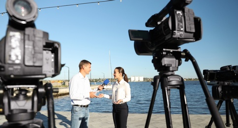 Professional journalist interviewing young woman near river on sunny day