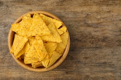 Bowl with tasty Mexican nachos chips on wooden table, top view. Space for text