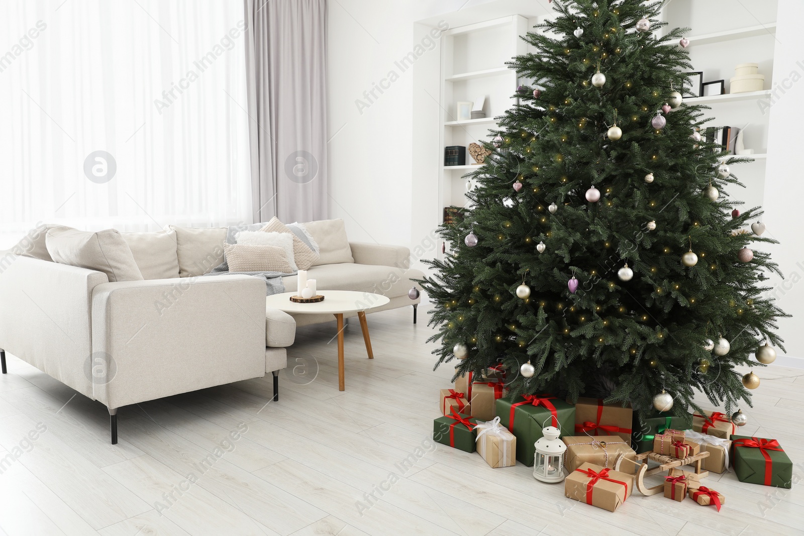 Photo of Beautifully wrapped gift boxes, wooden sleigh and lantern under Christmas tree in living room