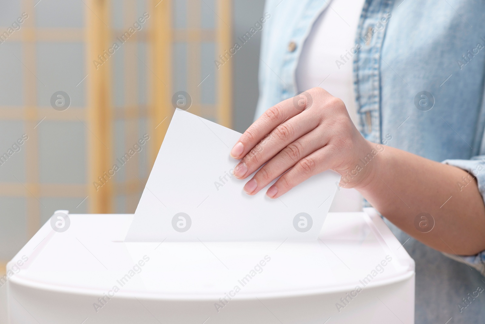 Photo of Woman putting her vote into ballot box on blurred background, closeup