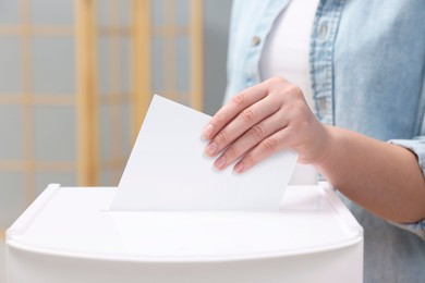 Photo of Woman putting her vote into ballot box on blurred background, closeup