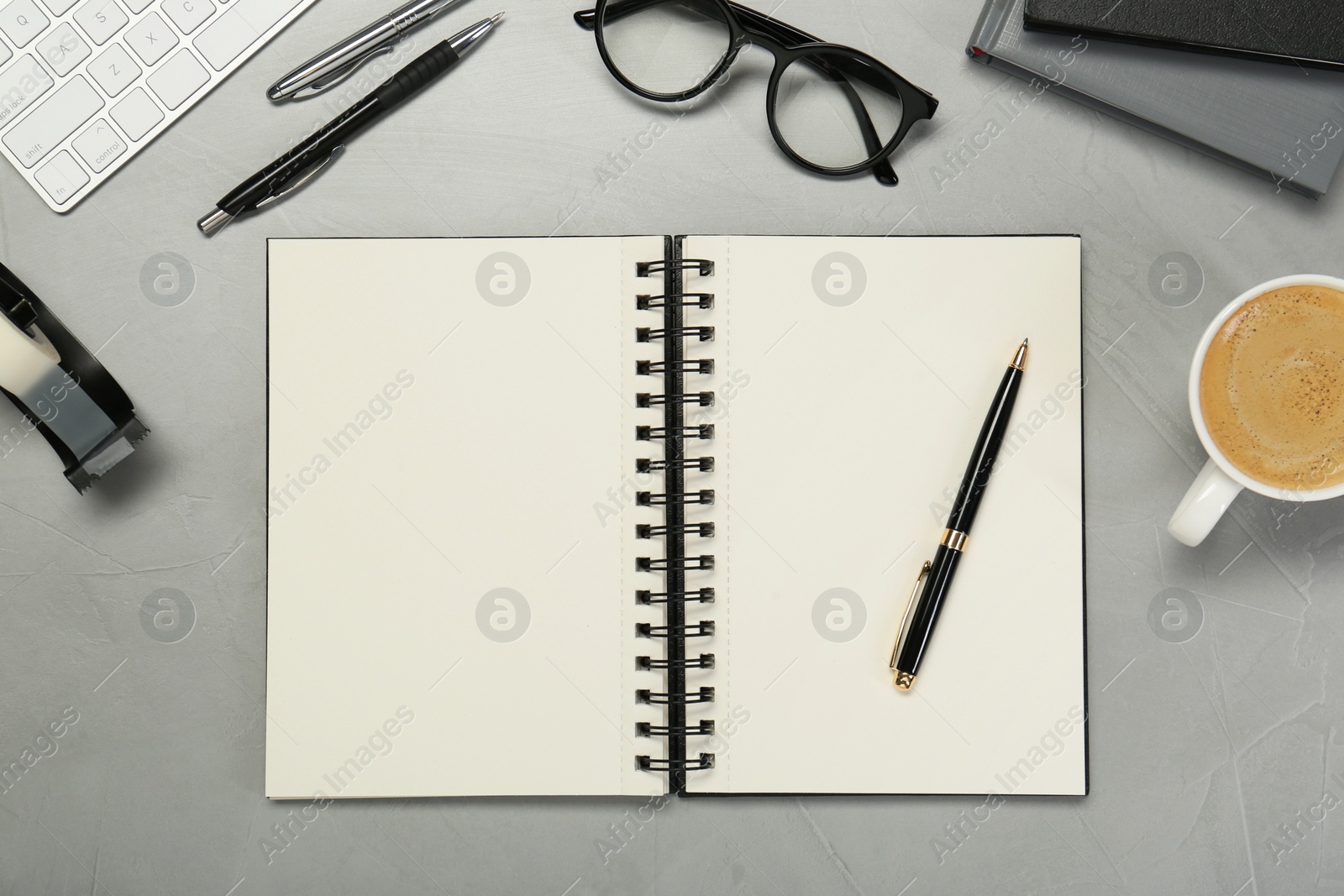 Photo of Open notebook, stationery, coffee and glasses on light grey table, flat lay