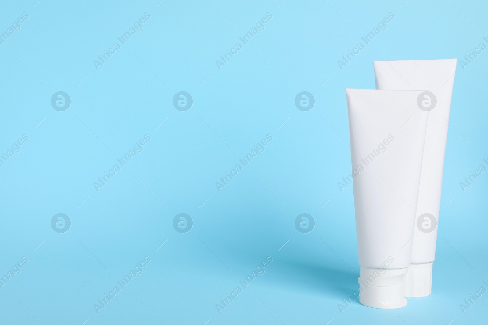 Photo of Blank tubes of toothpaste on light blue background. Space for text