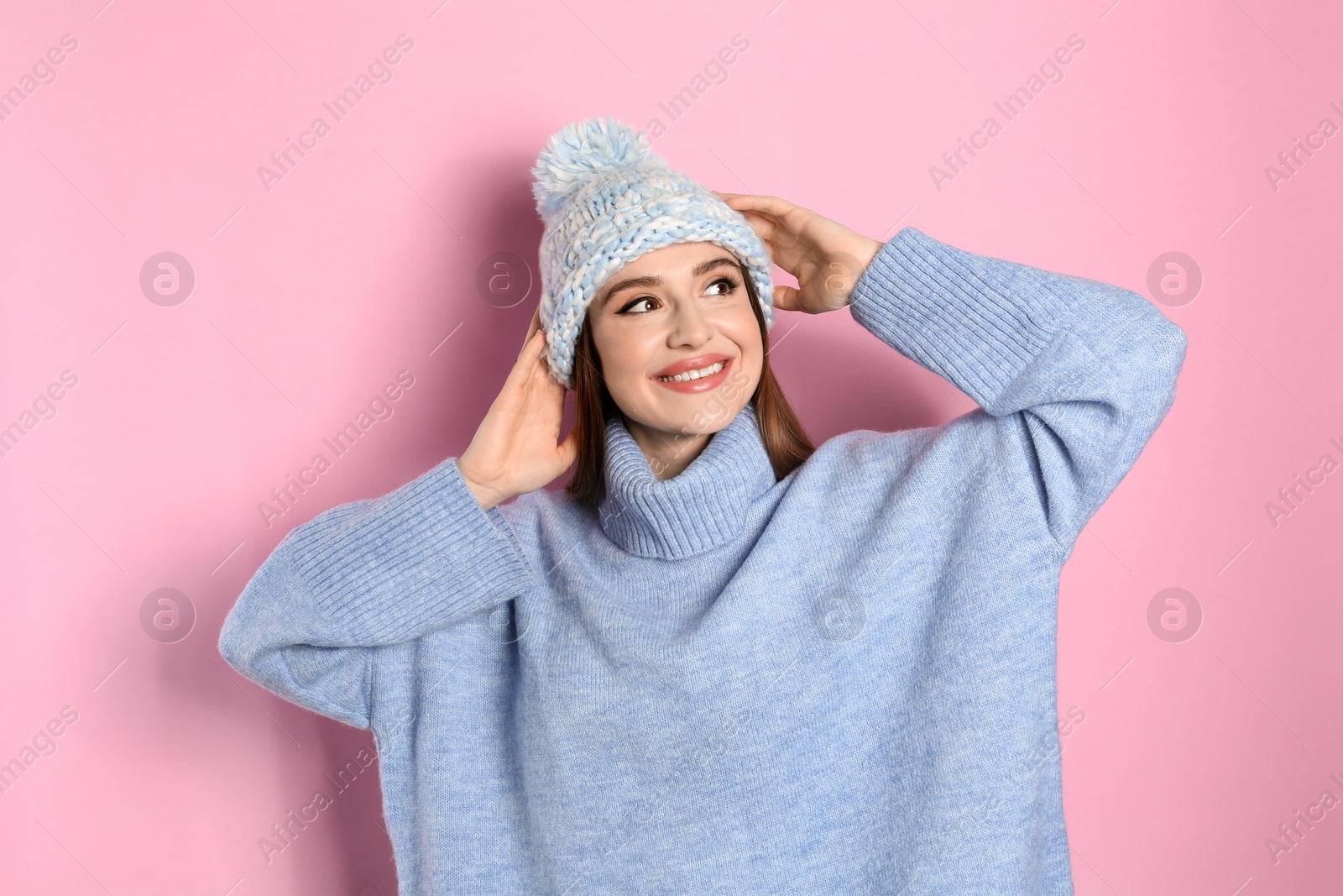 Photo of Young woman wearing warm sweater and hat on pink background. Winter season