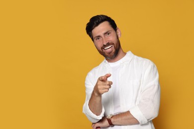 Smiling bearded man pointing forward finger on orange background. Space for text