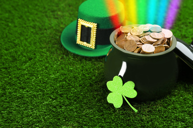 Pot with gold coins, hat and clover on green grass, space for text. St. Patrick's Day celebration