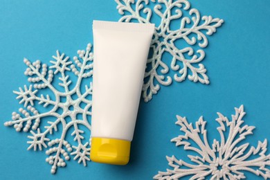 Tube of hand cream and snowflakes on light blue background, flat lay. Winter skin care