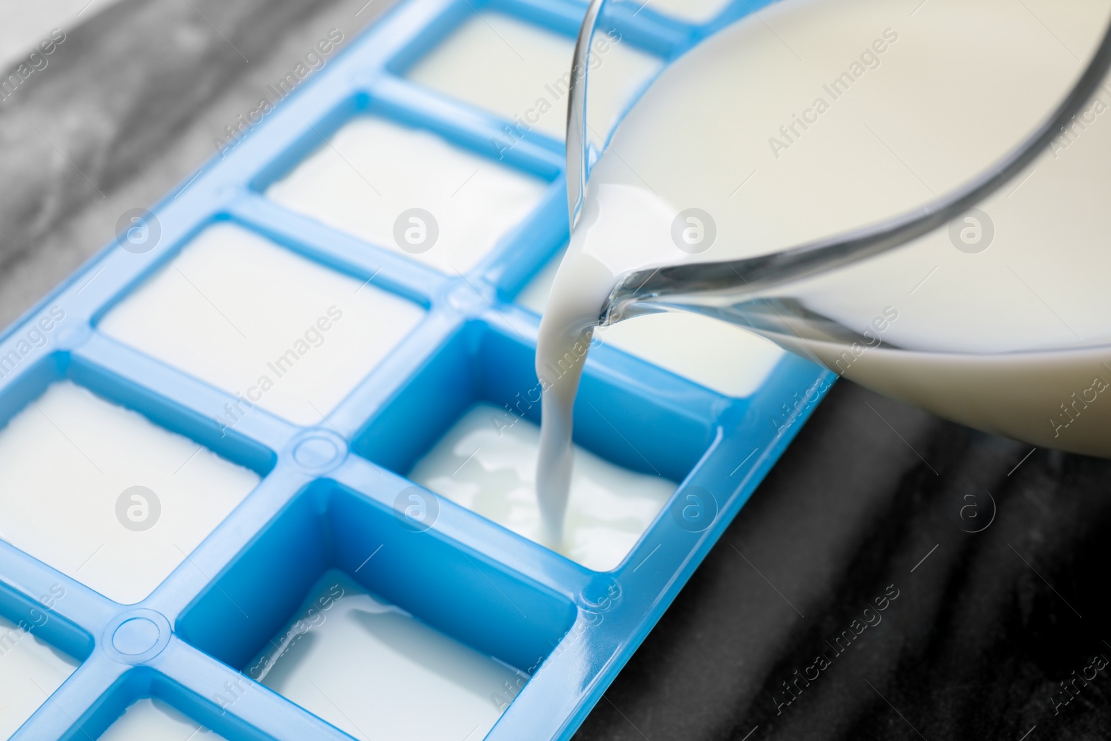 Photo of Pouring milk into ice cube tray at table, closeup