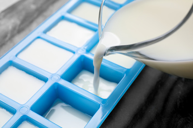Pouring milk into ice cube tray at table, closeup