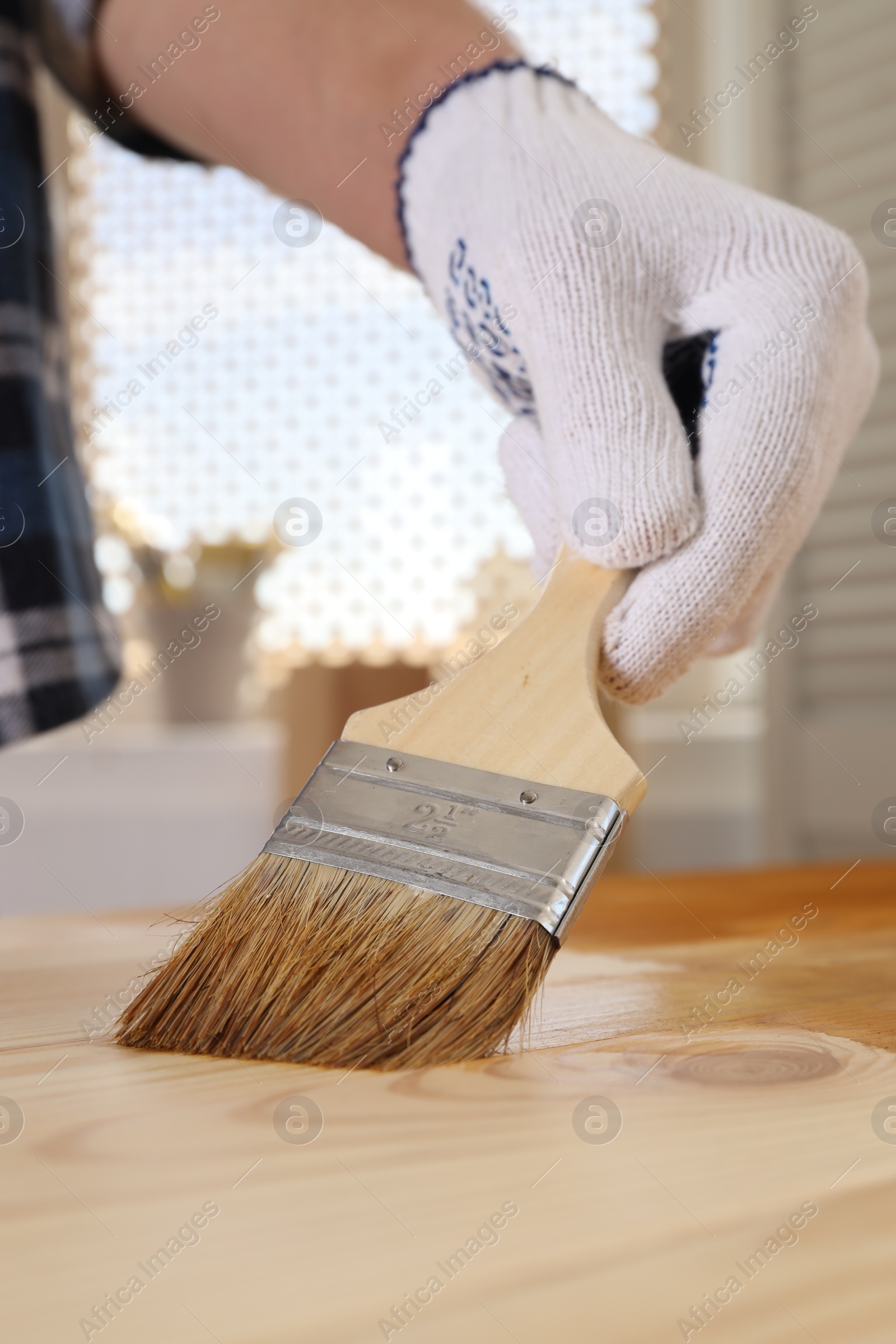 Photo of Man with brush applying wood stain onto wooden surface indoors, closeup