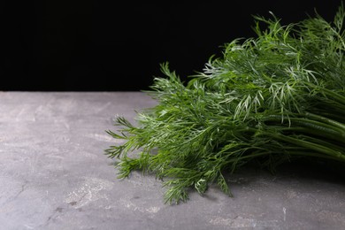 Photo of Sprigs of fresh dill on grey textured table against black background, closeup. Space for text