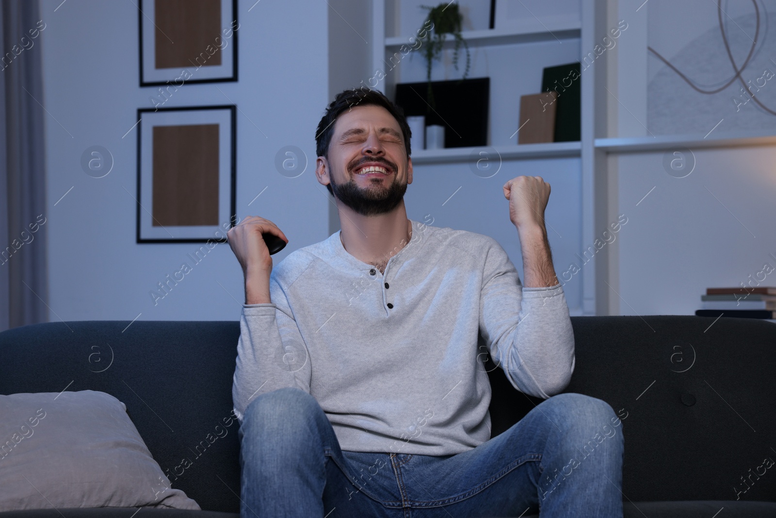 Photo of Emotional man with remote controller watching tv at home