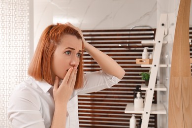 Photo of Emotional woman suffering from baldness near mirror at home