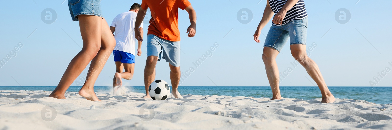 Image of Group of friends playing football on sandy beach, low angle view. Banner design