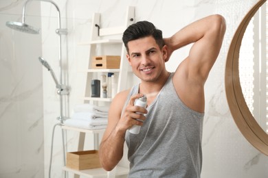 Handsome man applying deodorant to armpit in bathroom, space for text