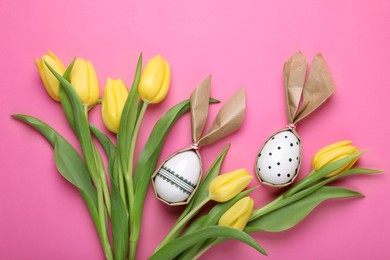 Easter bunnies made of craft paper and eggs among beautiful tulips on pink background, flat lay