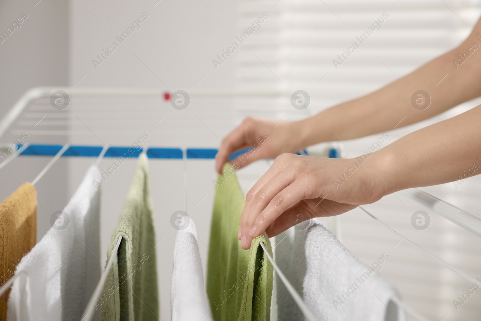 Photo of Woman hanging clean terry towels on drying rack indoors, closeup