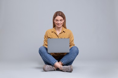 Happy woman with laptop on light grey background