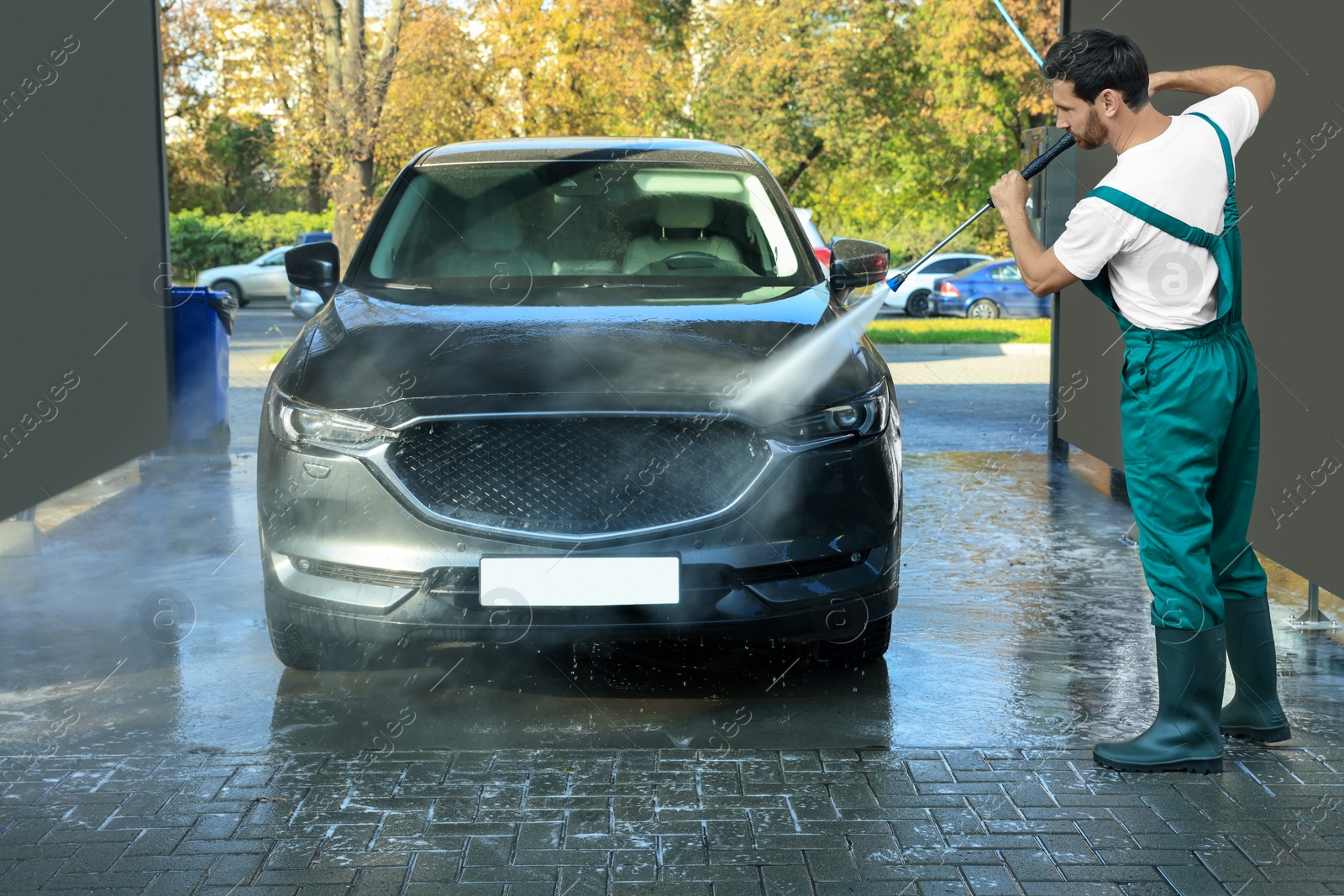 Photo of Worker washing auto with high pressure water jet at outdoor car wash