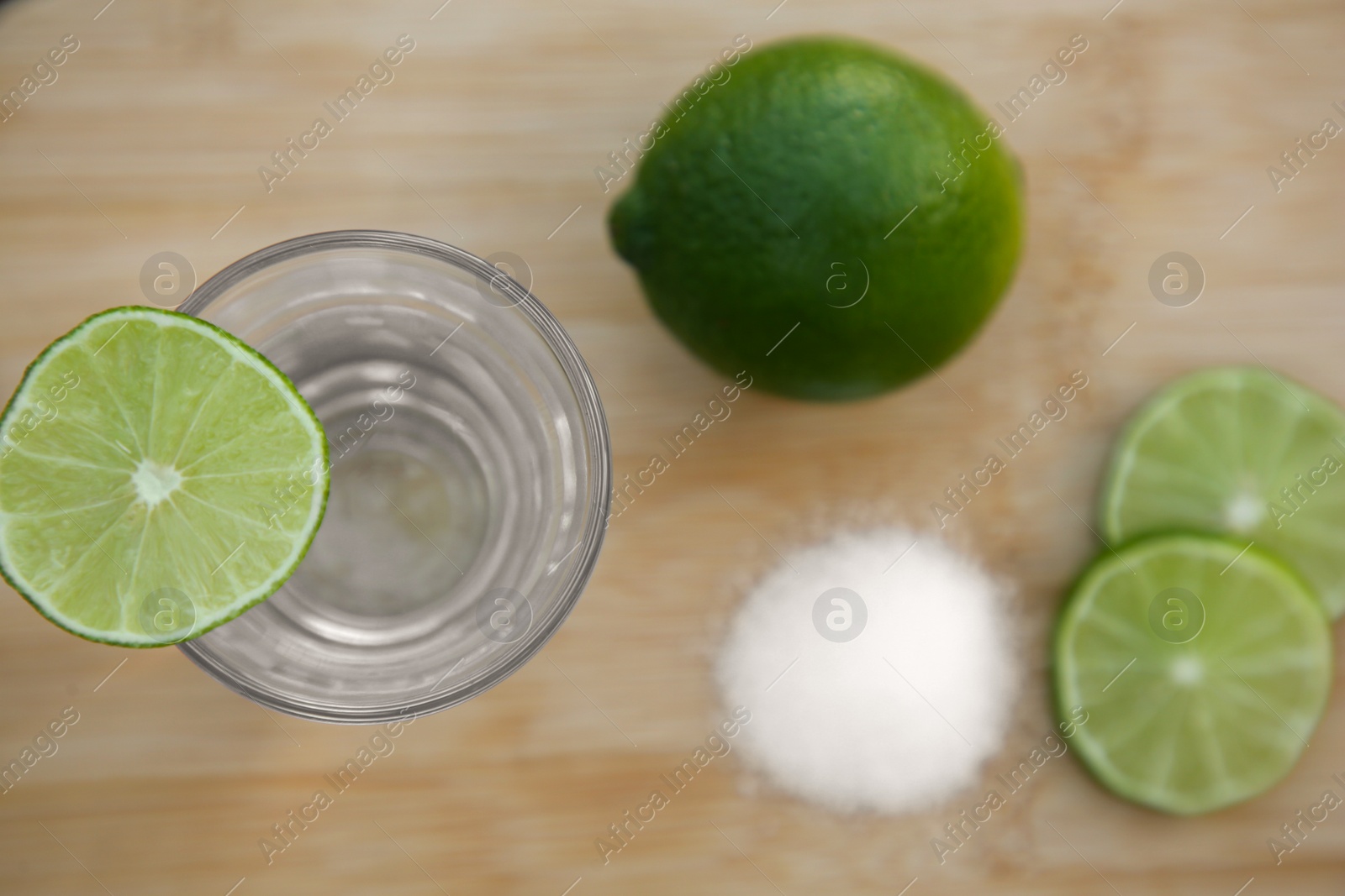 Photo of Mexican tequila shot with lime slices on wooden table, flat lay. Drink made from agave