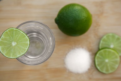 Mexican tequila shot with lime slices on wooden table, flat lay. Drink made from agave