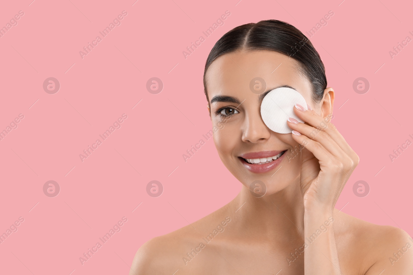 Photo of Beautiful woman removing makeup with cotton pad on pink background. Space for text
