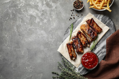 Delicious grilled ribs served on grey table, flat lay. Space for text