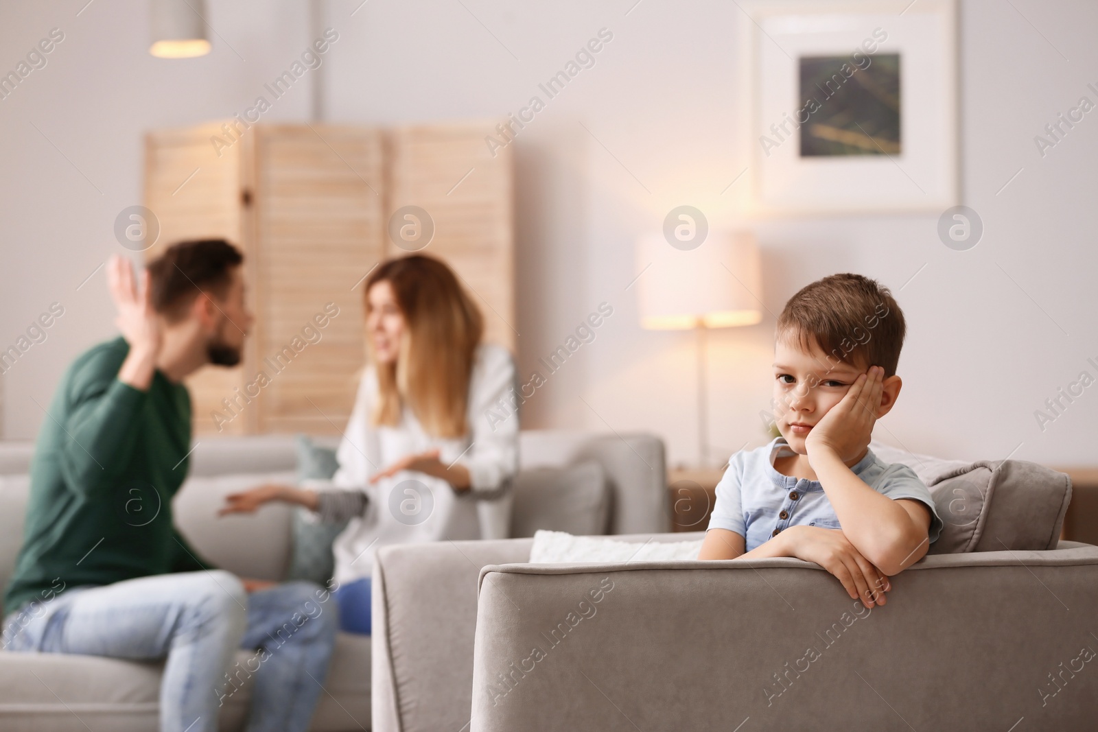 Photo of Little unhappy boy sitting in armchair while parents arguing at home