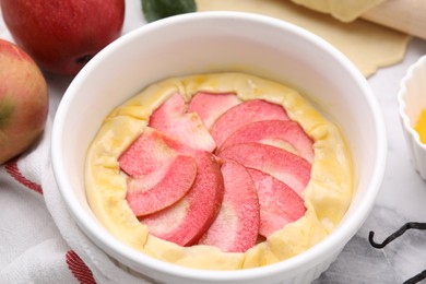 Photo of Baking dish with fresh dough and apples on white table, closeup. Making galette