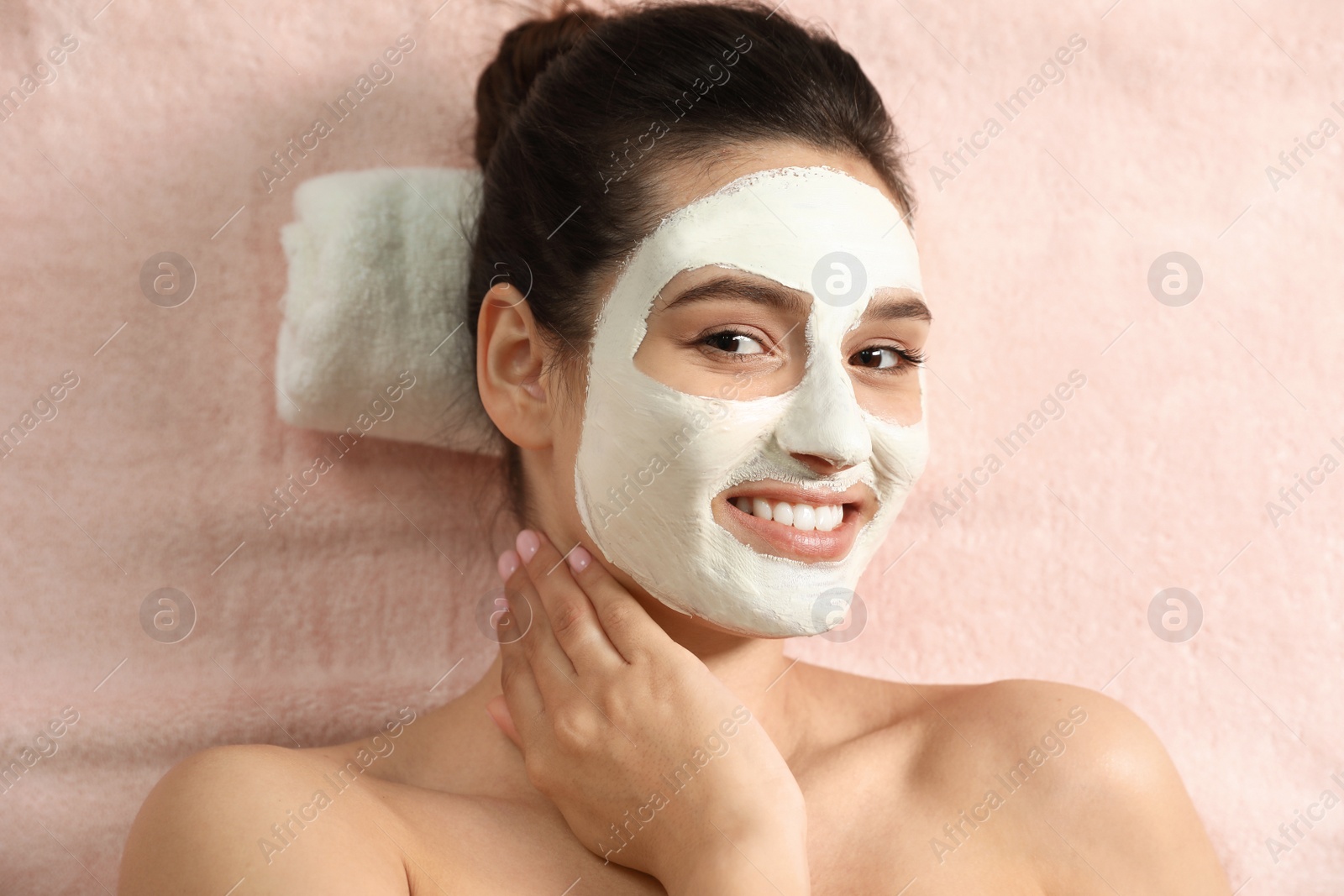 Photo of Beautiful woman with white mask on face relaxing in spa salon, top view